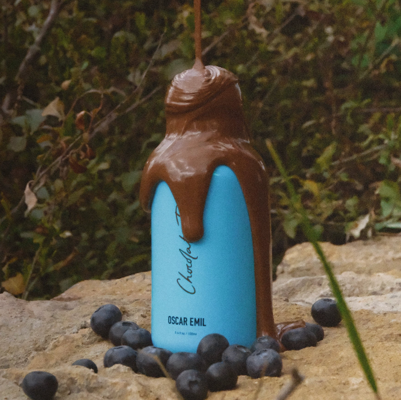 Blue bottle with chocolate being poured over it, surrounded by blueberries on a natural background