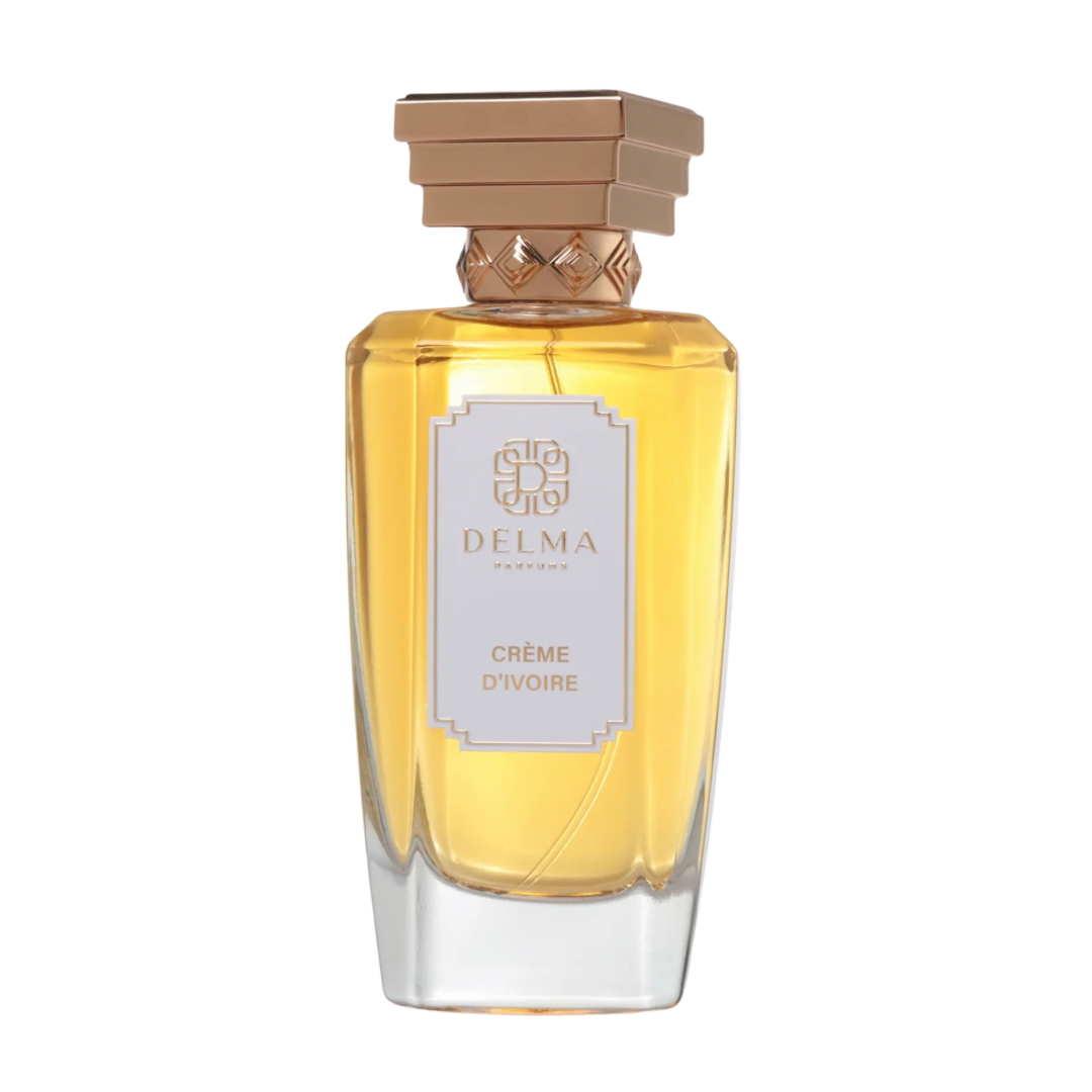 A bottle of Delma Crème D'ivoire perfume with a clear glass body showing the golden-yellow liquid inside, a white label with gold lettering, and a metallic gold cap, isolated on a white background.