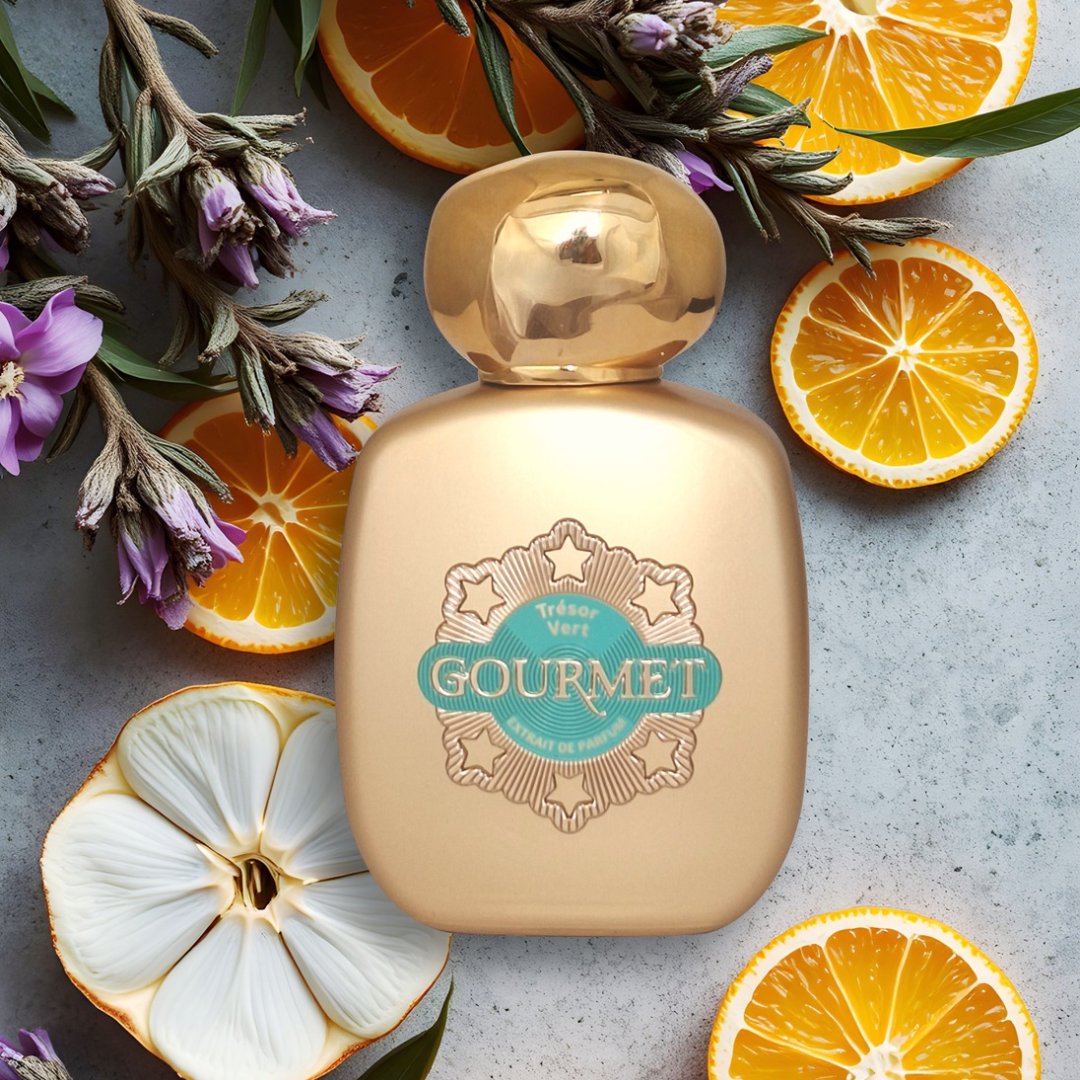 Gold perfume bottle labeled 'Gourmet' surrounded by orange slices and flowers on a gray surface