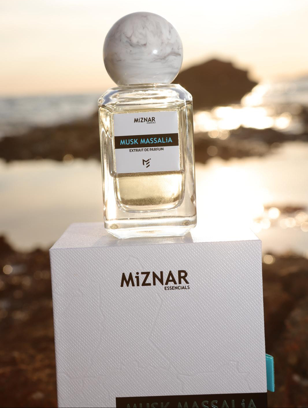 Miznar Musk Massalia perfume bottle with packaging on a beach at sunset