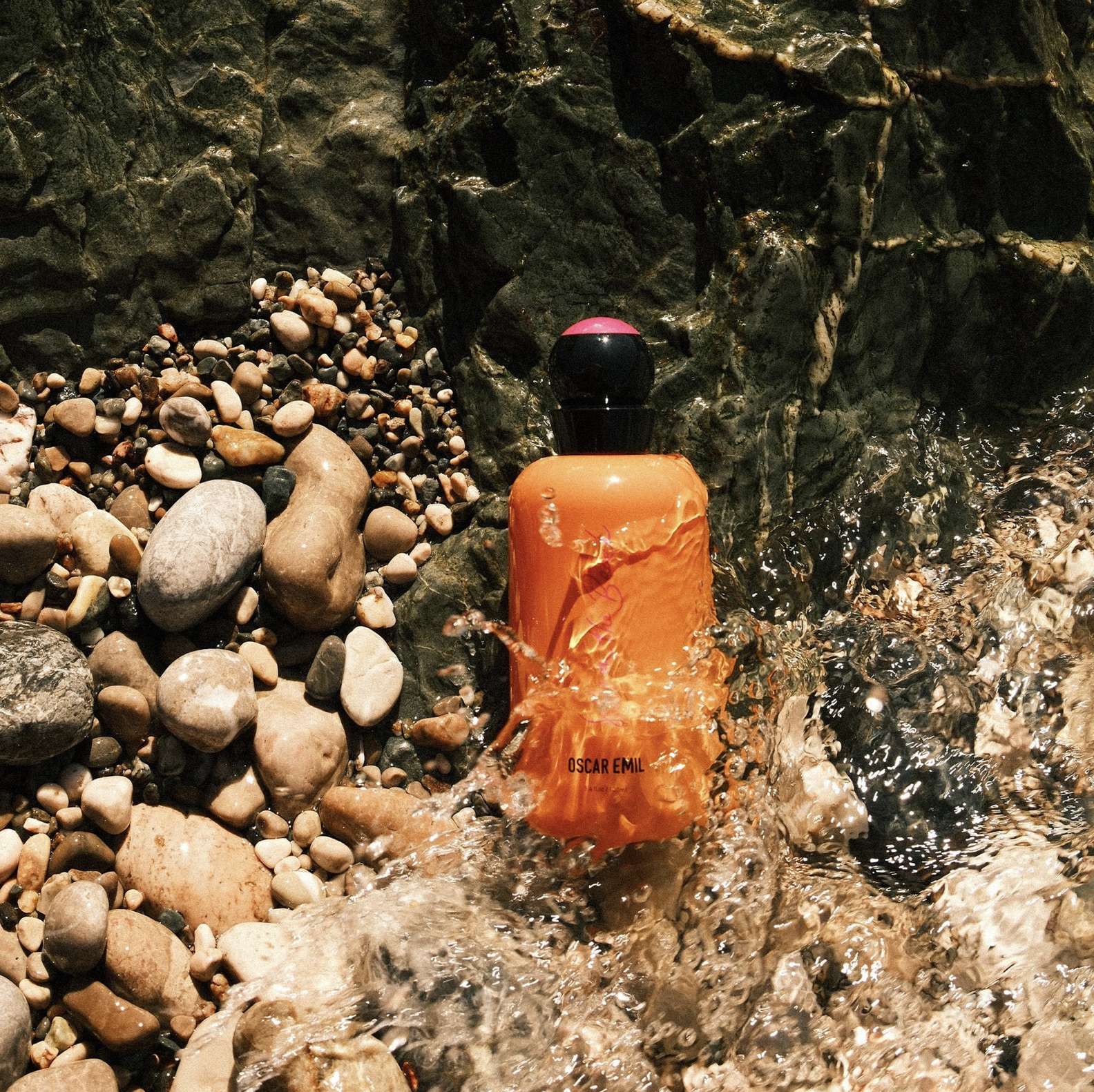 Orange bottle with black cap on a rocky surface with water splashing around it