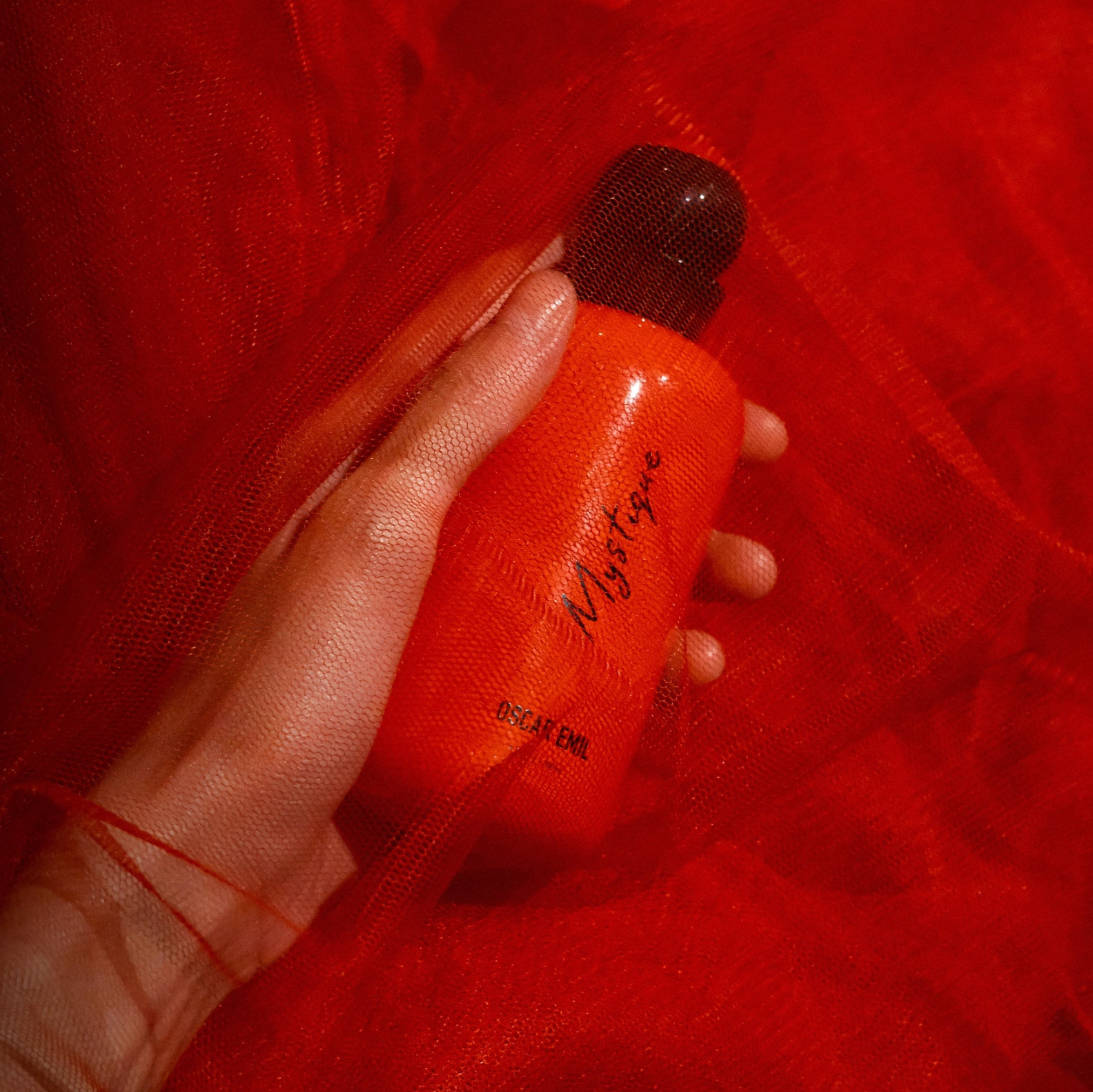 Hand holding a red bottle labeled 'Mystique' against a red background