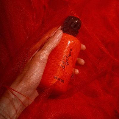Hand holding a red bottle labeled 'Mystique' against a red background
