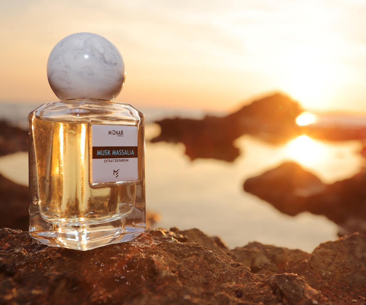 Perfume bottle on a rocky surface with a sunset in the background