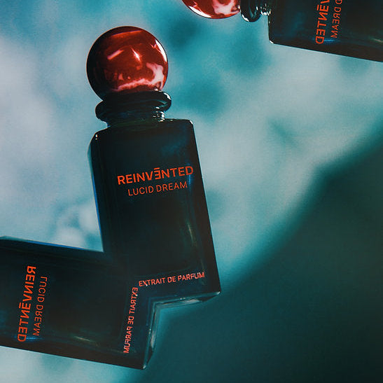 Perfume bottles with red caps and 'Reinvented' branding on a blurred background