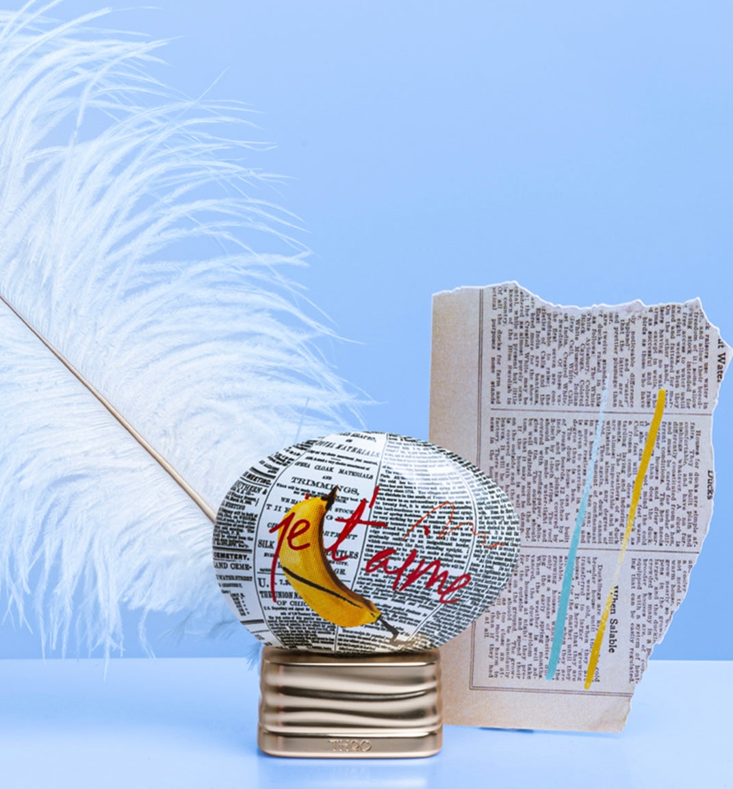 A bottle of 'The House Of Oud L'EXPLICITE Eau de Parfum 2.5 oz Unisex' with a newspaper wrapped around it, placed on a stand, with a piece of paper art in the background.