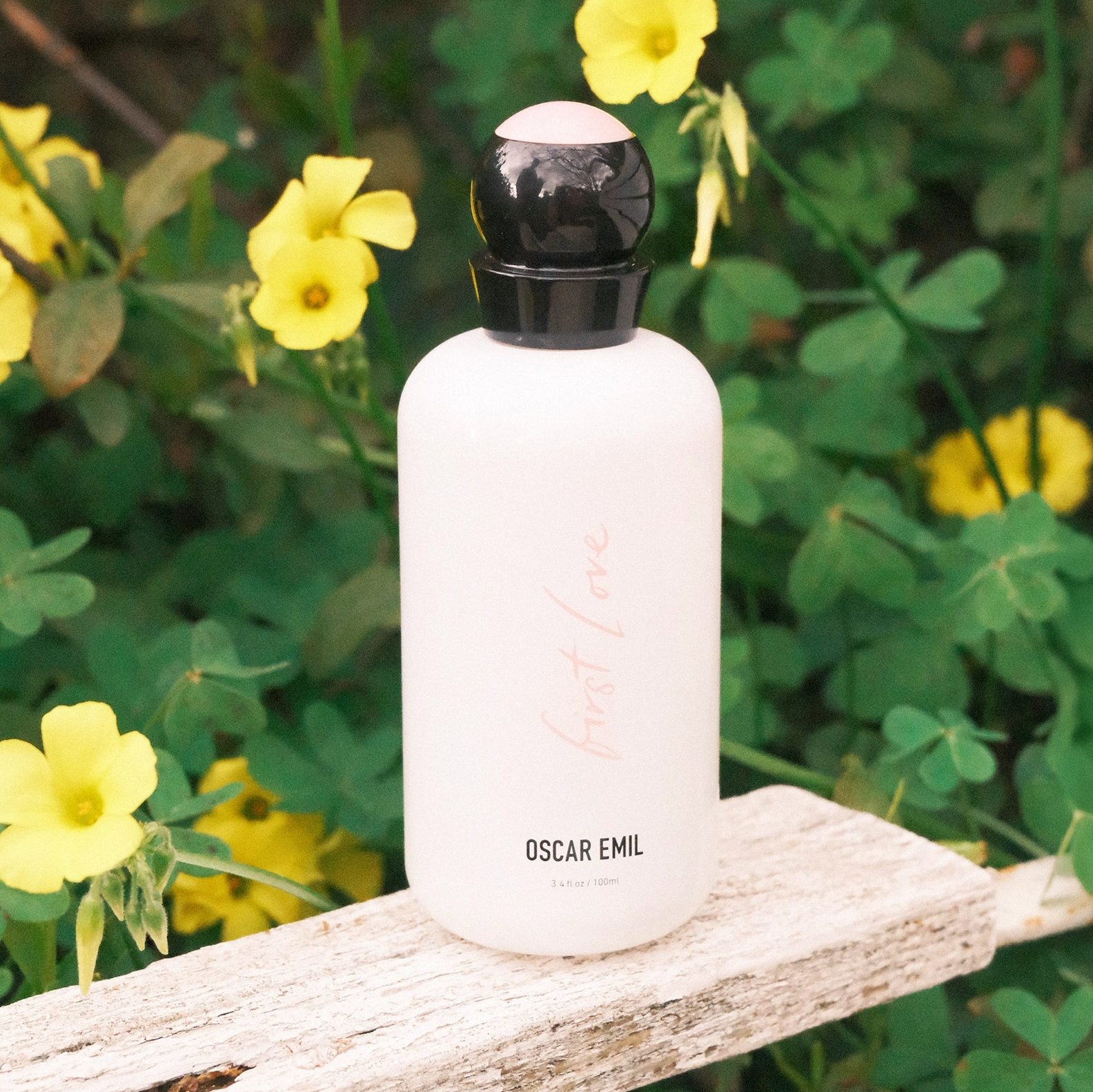 White bottle with black cap on a wooden surface surrounded by yellow flowers and green foliage