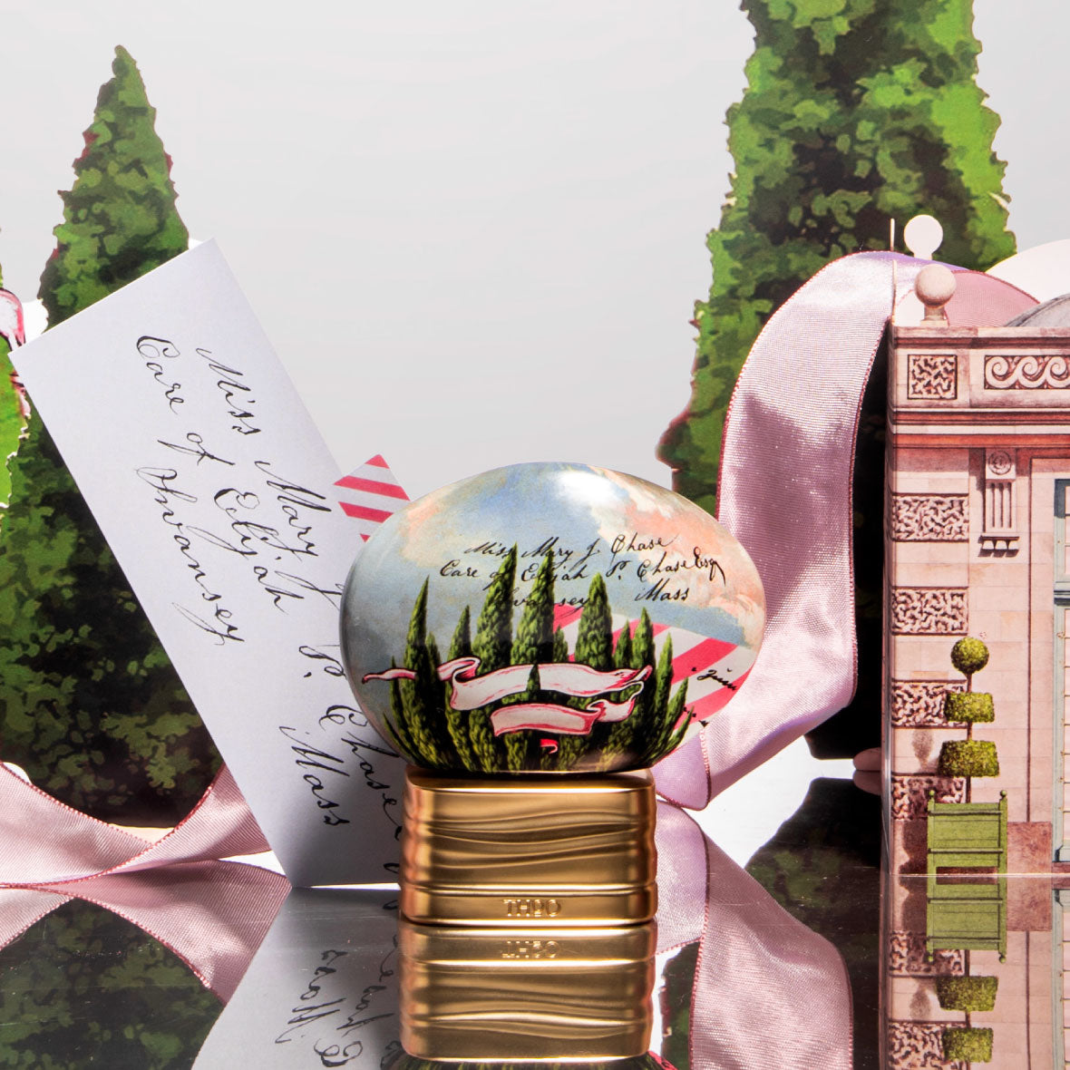 Decorative bottle with a scenic design on a reflective surface with greenery and a pink ribbon in the background.