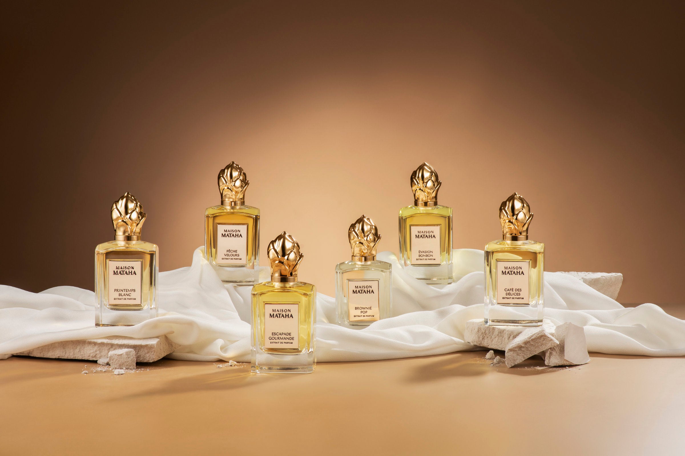 Five gold and white perfume bottles on a beige background